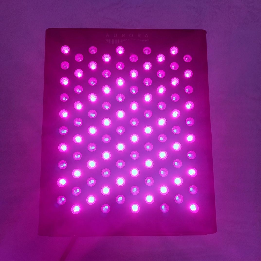 Ein LED-Panel mit einem Gitter aus leuchtend rosa Lichtern, das ein leuchtendes, farbenfrohes Display erzeugt. Die Oberseite trägt die Aufschrift AURORA.