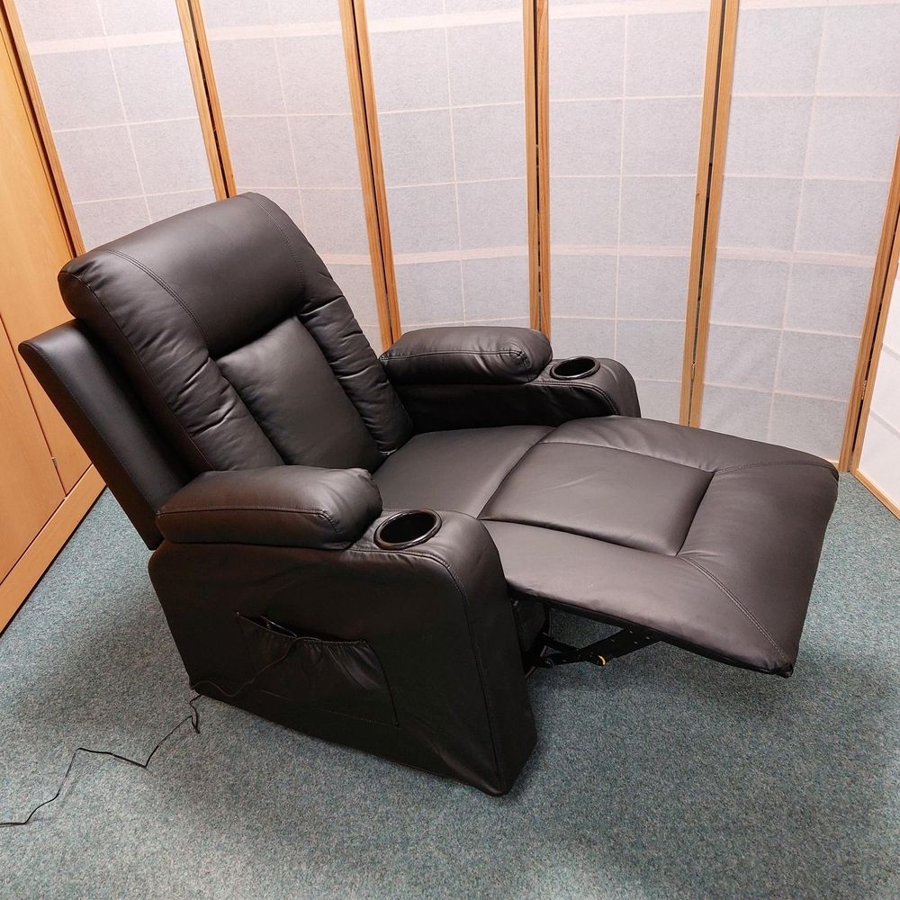 Ein schwarzer Ledersessel mit Getränkehaltern, teilweise zurückgelehnt, vor einem Hintergrund aus Holzpaneelen und Teppichboden.